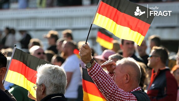 Mann hält am Tag der Deutschen Einheit die Nationalfahne hoch.