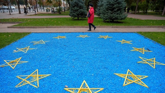 Eine Frau geht an einer EU-Flagge aus blauen Kieselsteinen vorbei