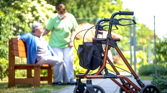 Ein Rollator steht nahe einer Pflegefachkraft und einer Bewohnerin eines Seniorenheims im Freien. 
