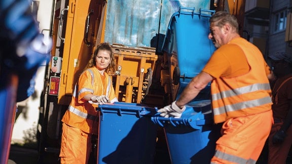 Mitarbeiter der Müllabfuhr schieben mehrere Papierabfalltonnen zur Schüttung des Abfallsammelfahrzeugs
