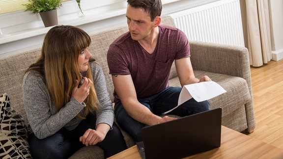Ein Mann und eine Frau sitzen in einer Wohnung zusammen an einem Laptop