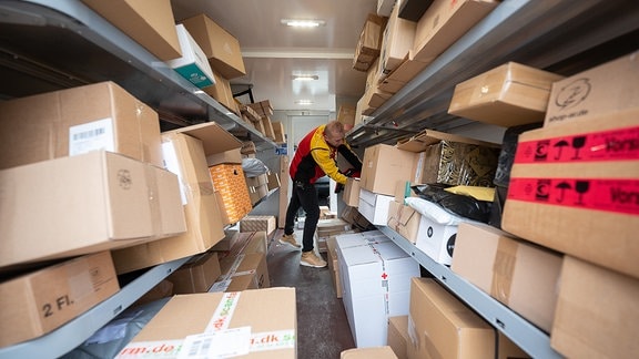 Ein DHL-Mitarbeiter sortiert in seinem Transporter Pakete und Päckchen