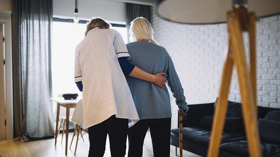 Krankenschwester stützt eine Seniorin beim laufen