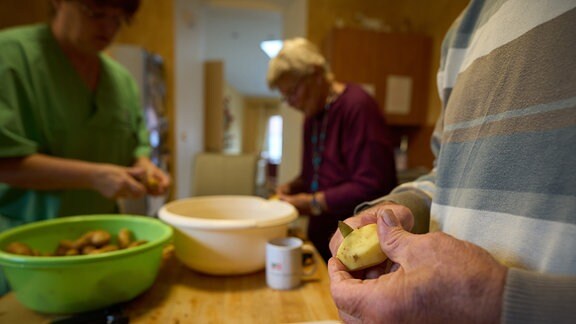 Ältere und eine Pflegeperson schälen Kartoffeln fürs Mittagessen