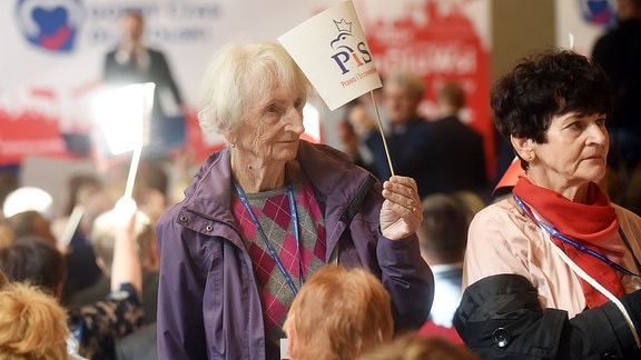 Eine ältere Frau hält ein Fähnchen hoch.