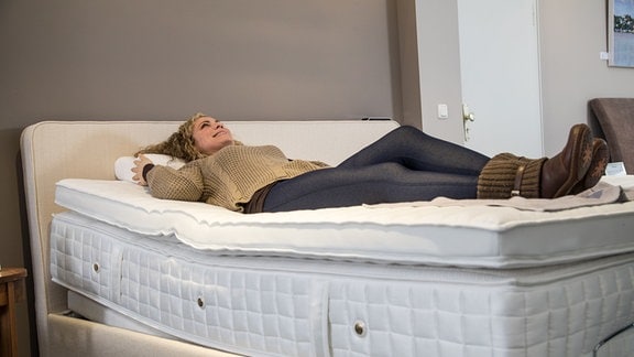 Gestelltes Foto einer Frau, die in einem Bettenhaus eine Matratze testet.