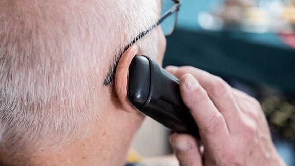 Ein älterer Menschen sitzt in seiner Wohnung und telefoniert mit einem Mobiltelefon.