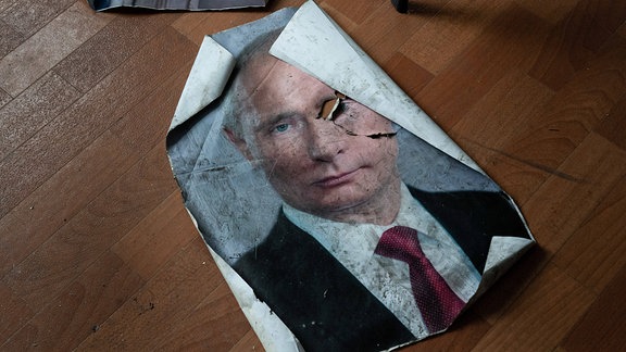 Ein Poster mit dem Bild des russischen Präsidenten Wladimir Putin liegt 2022 beschädigt auf dem Boden einer Polizeistation.