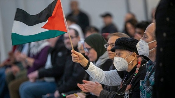 Eine Frau in einem Publikum schwenkt die palästinensische Flagge.