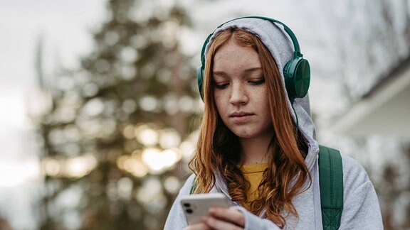 Porträt einer Teenagerin, die auf ihr Smartphone schaut.
