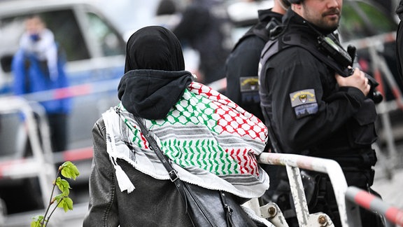 Eine Aktivistin mit Kufiya geht vor der Veranstaltungshalle des Palästina-Kongress 2024 an einer Polizeisperre entlang.