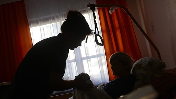 Eine Frau wird in einem Seniorenpflegeheim in ihrem Bett in ihrem Zimmer von einer Pflegerin betreut.