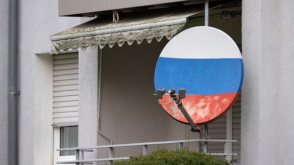 Eine Satellitenschüssel, die in den Farben der russischen Flagge angemalt ist, hängt an einem Haus.