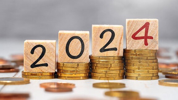 Die Jahreszahl 2024 auf Holzwürfeln auf Münzgeld Stapeln