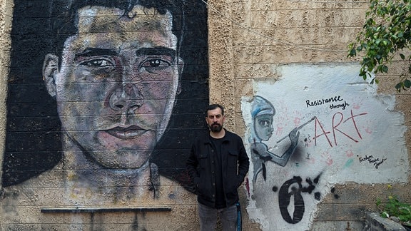 Der Palästinenser Ahmed Tobasi, der künstlerische Leiter des Freedom Theatre, das von Zakaria Zubeidi, einem Anführer der al-Aqsa-Märtyrerbrigaden im Westjordanland, mitbegründet wurde, posiert für ein Foto vor Graffiti, das Zubeidi im Freedom darstellt.