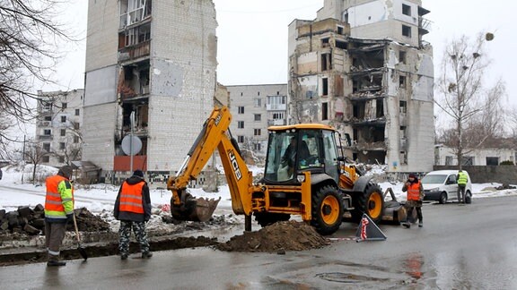 Mitarbeiter eines Versorgungsunternehmens arbeiten vor einem durch russischen Beschuss zerstörten mehrstöckigen Gebäude in der Tsentralna-Straße im Norden der Zentralukraine.