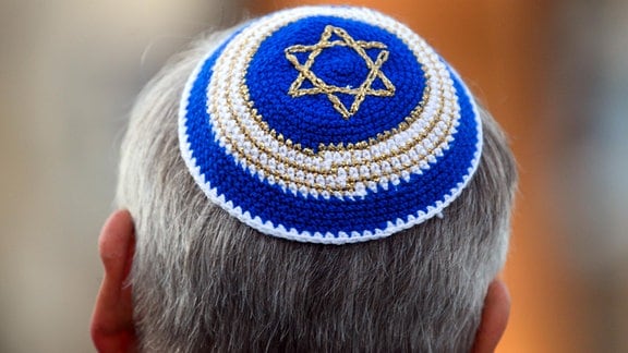 Ein Mann trägt im Rahmen einer Kranzniederlegung vor der Synagoge eine Kippa mit Judenstern.