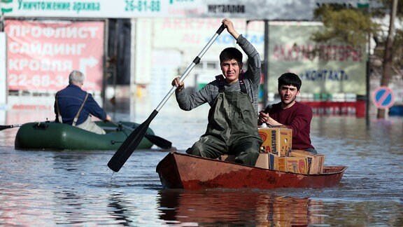 Zwei Männer rudern ein Boot durch das Hochwasser eines überschwemmten Gebiets, um Lebensmittel auszuliefern.