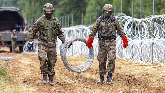 2 Soldaten ziehen einen Stacheldrahtzaun. Grenze zwischen Polen und Belarus.