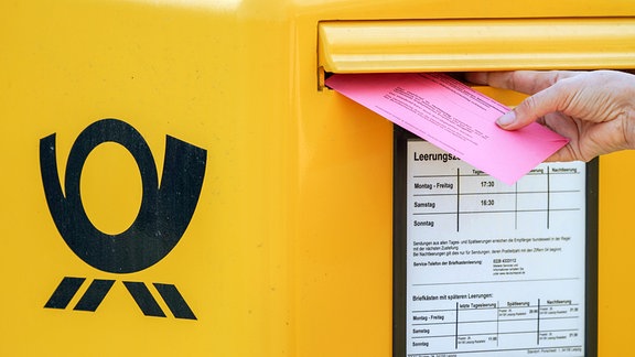 Einen Briefwahlumschlag zur Bundestagswahl 2021 steckt eine Frau in einen Briefkasten.