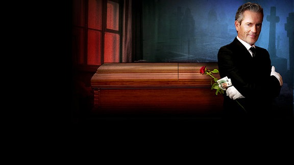 Schauspieler auf Symbolbild: Ein Mann im schwarzen Anzug steht vor einem Sarg, er hält eine Rose und Geld in der Hand, er trägt weiße Handschuhe. Im Hintergrund ist eine Friedhofsszene angedeutet.