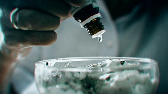 Eine Frauenhand tropft ein Medikament auf Eis in einer Glasschale (Nachstellung).