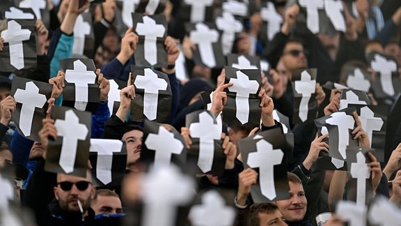 Fußballfans im Stadion harten schwarze Zettel mit Totenkreuzen in die Luft