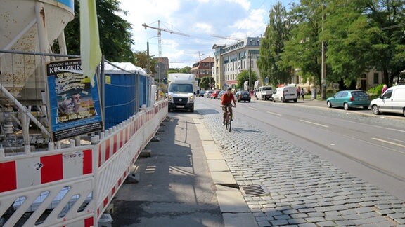 Radfahrer fährt neben einer Baustelle auf einer Kopfsteinpflaster-Straße