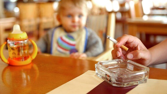 Ein kleines Kind schaut seinen Eltern beim Rauchen zu.