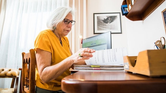 Eine Seniorin sitzt an einem Schreibtisch