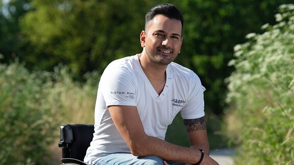 Tan Caglar in weißem T-Shirt und Jeans auf einem Parkweg im Rollstuhl