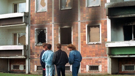 Eine Gruppe junger Männer vor einem Plattenbau mit Spuren eines Brandes 