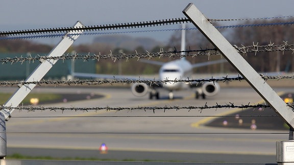 Symbolfoto ein Flugzeug auf einer Landebahn hinter Stacheldraht