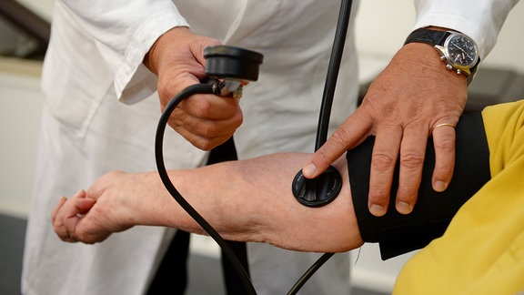Ein Arzt misst in einer Praxis einer Patientin den Blutdruck.