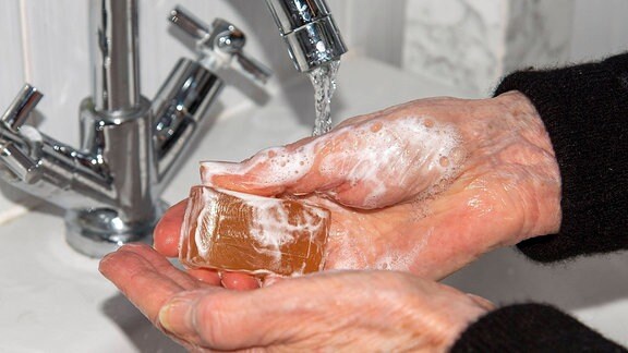 Die Hände einer Seniorin unter einem Wasserhahn