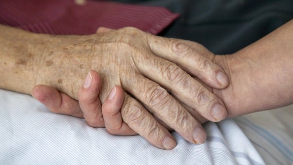 Die Hand einer Pflegerin hält die Hand eines sterbenden Mannes