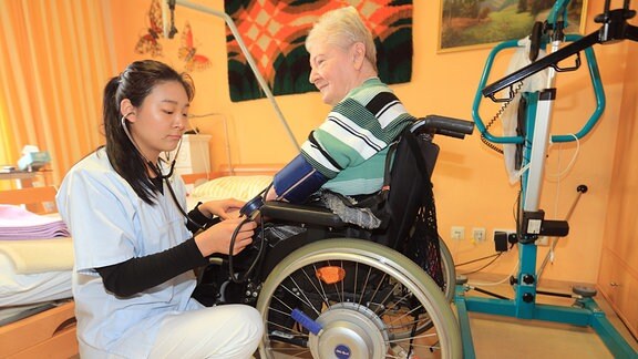 Mulin Lin (l), Pflegeassistentin aus China, misst den Blutdruck einer Rentnerin im Seniorenzentrum der Arbeiterwohlfahrt (AWO) in Magdeburg