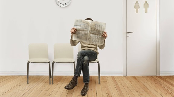 Eine Person in einem Wartezimmer mit Zeitung vor dem Gesicht.