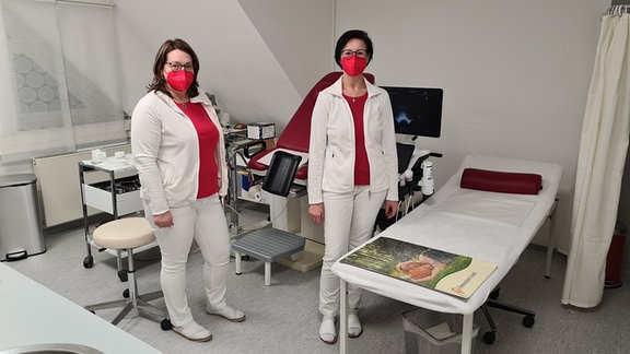 Zwei Frauen stehen in einem Behandlungsraum mit Frauenarzt-Untersuchungsstuhl.