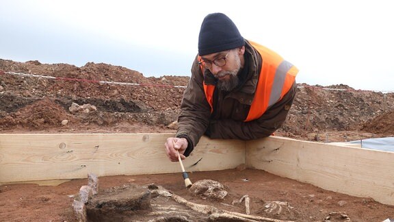 Ein Mann beugt sich über Knochen in einer Grabstelle