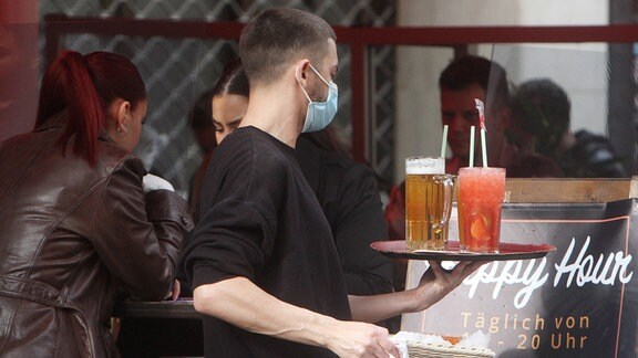 Ein Kellner mit Maske trägt ein Tablett mit Getränke