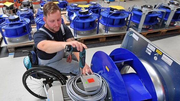 An einem Arbeitsplatz für Motorklemmen ist ein Mitarbeiter im Rollstuhl mit Montagearbeiten beschäftigt. 
