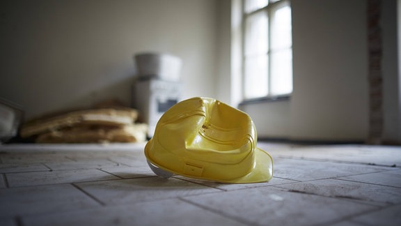 Ein gelber kaputter Bauhelm leigt auf dem Boden einer Baustelle