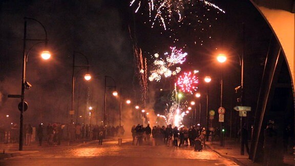 Dutzende Menschen feiern Silvester auf der Sternbrücke in Magdeburg. Im Hintergrund erleuchtet Feuerwerk