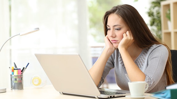 Eine Frau schaut gelangweilt auf Laptop-Bildschirm.