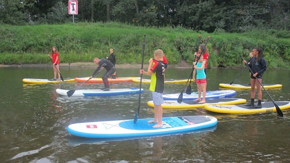 Kinder paddeln auf Brettern auf einem Fluss