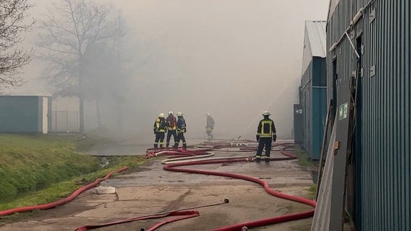 Feuerwehrmänner löschen in dichtem Rauch eine Lagerhalle.