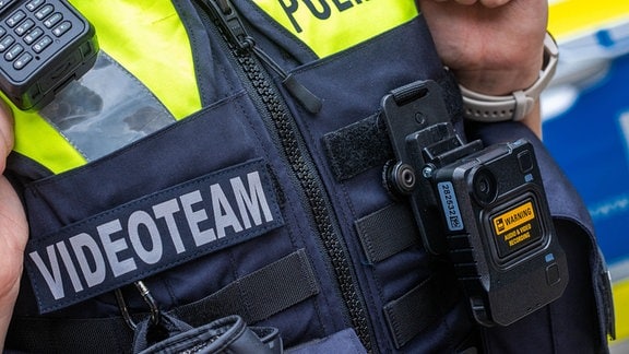 Eine neue Body-Cam hängt an der Schutzweste einer Polizeibeamtin.
