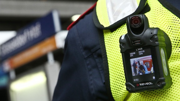 An der Weste eines Sicherheitsmitarbeiters der Deutschen Bahn hängt eine Bodycam. 