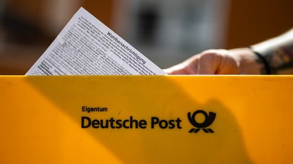 Ein Briefträger der Deutschen Post hält eine Wahlbenachrichtigung in einer Hand.